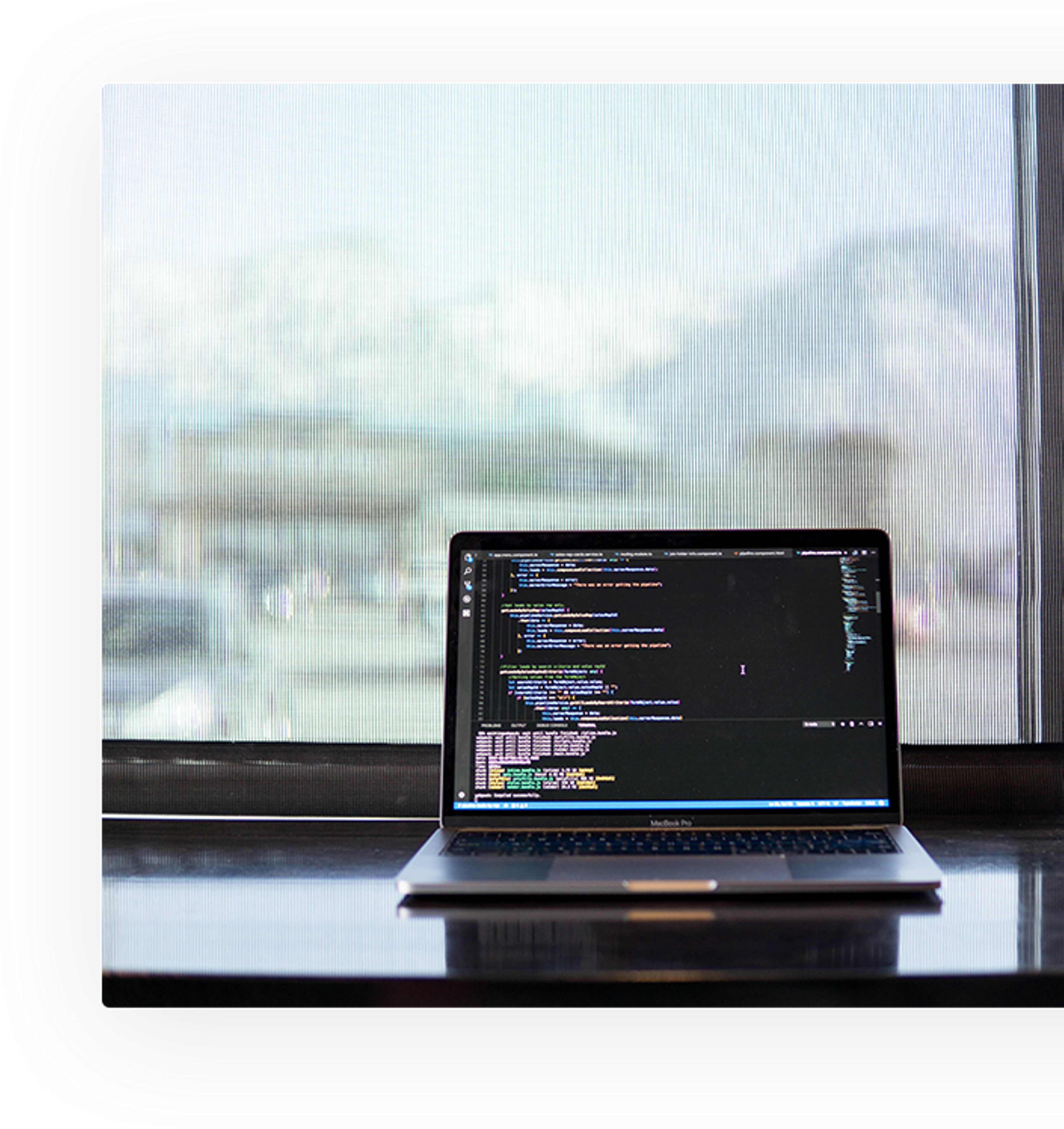 Laptop with open code editor showing active programming in front of a window with mountains in the background